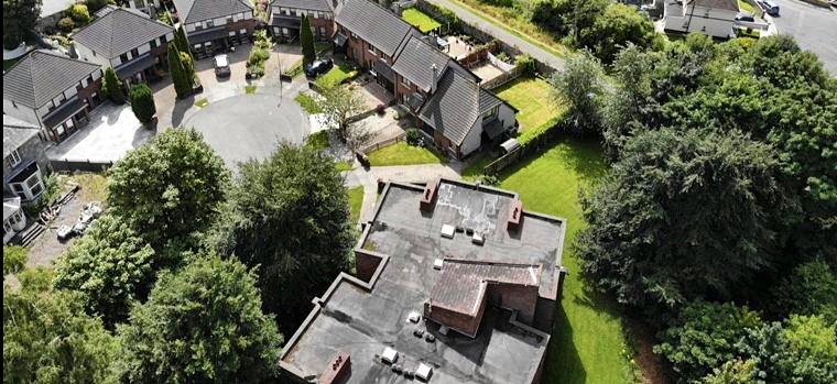 Aerial view of the flat roofed apartment block in the foreground, with the houses and their shared parking court beyond