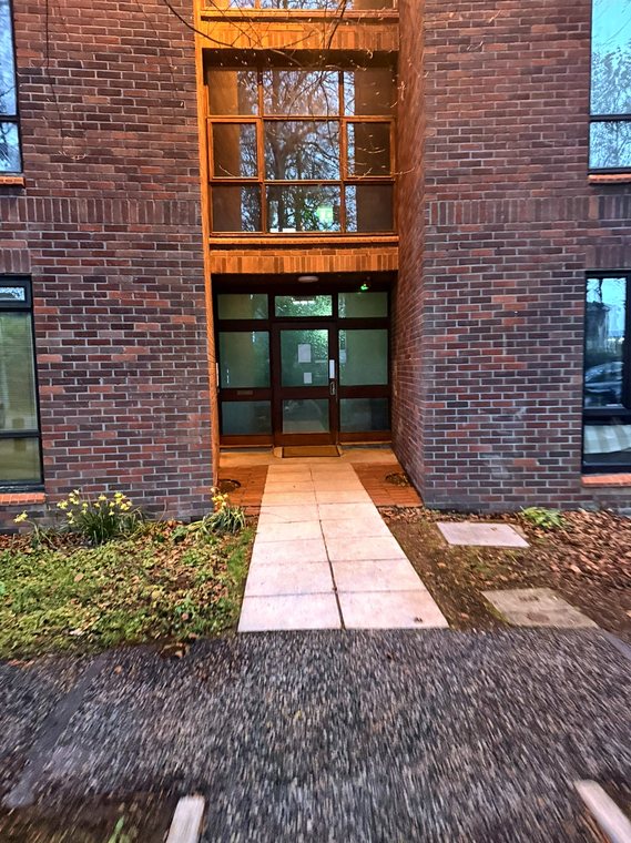 The lit main entrance of the apartment block at dusk, with the paved path leading to the door