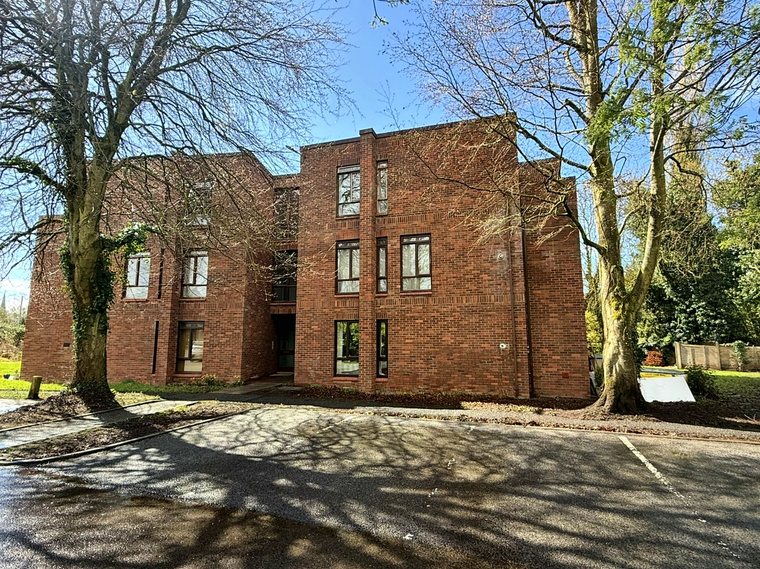 The front of the apartment block in sunshine, with tree shadows across the car park