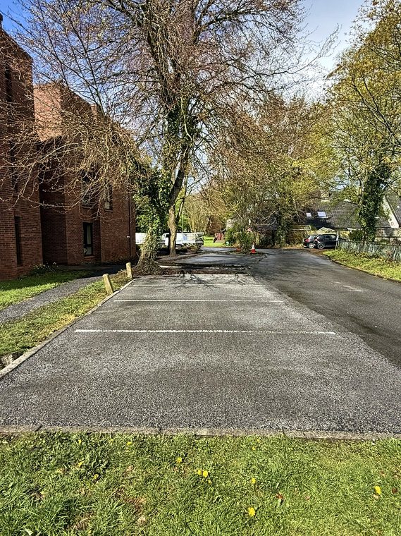 Marked parking spaces beside the apartment block, with trees and the access road beyond